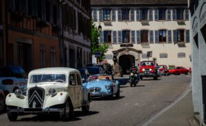 Colonne de véhicules anciens lors de la JNVE 2026 dans une rue d'un village d'Alsace.